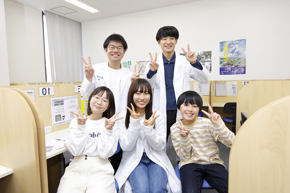 ピースで記念撮影をする3人のスタッフと2人の生徒