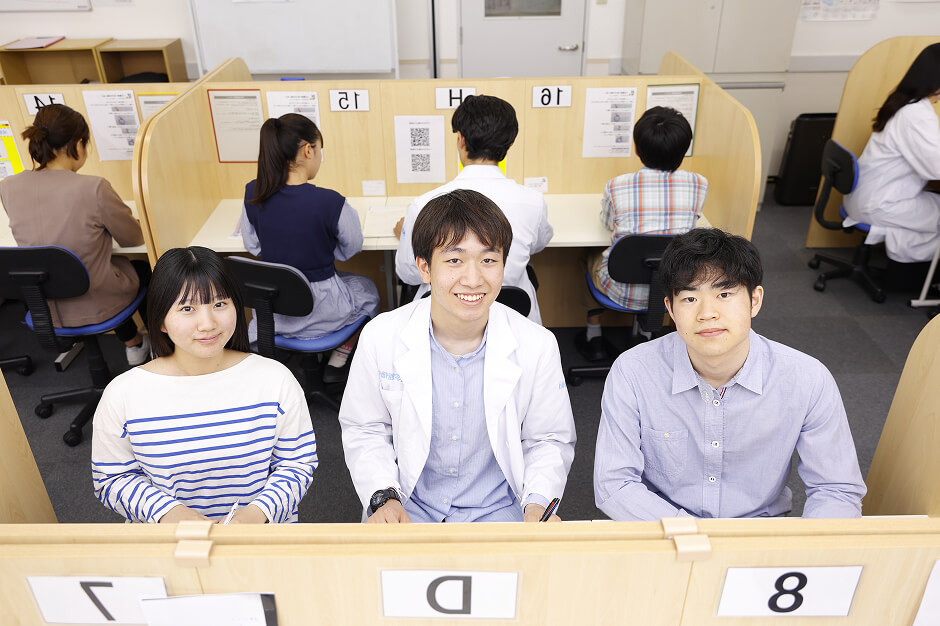 カメラに向かって笑顔の1人のスタッフと2人の生徒